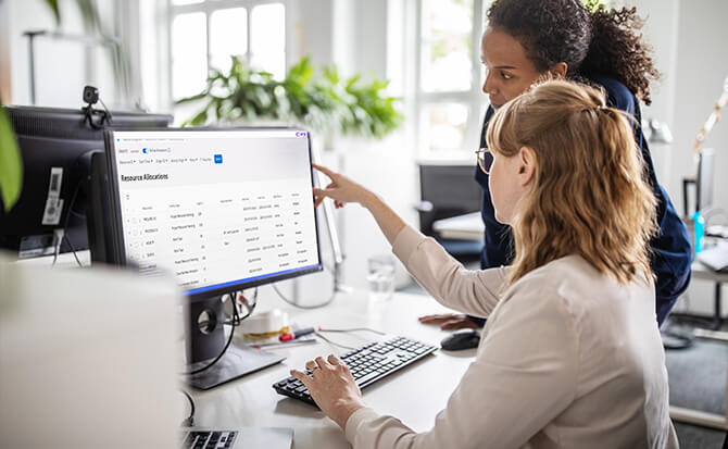 Due donne lavorano davanti a un computer, con una che indica lo schermo, utilizzando un software di Contact Center per ottimizzare la gestione e l'interazione con i client.