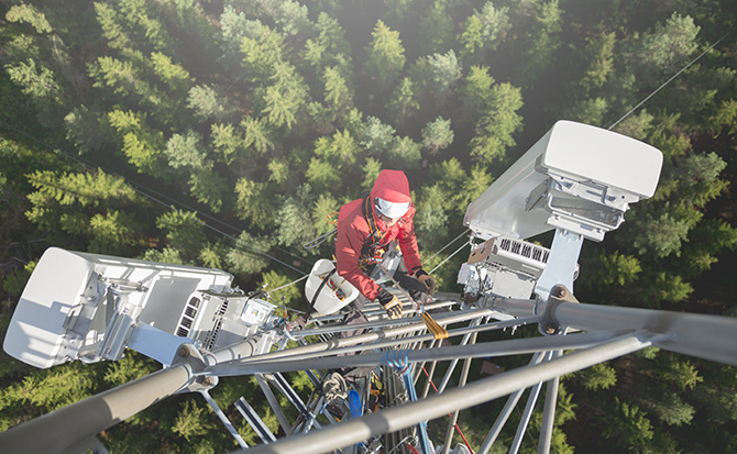 Telecommunication manual high worker engineer installing new 3g 4g LTE antenna on tall mobile base station (communication tower) in the middle of european forest, high angle of view. Working at height. Telecommunication masts and towers are typically tall structures designed to support antennas for telecommunications and broadcasting. Drone point of view.